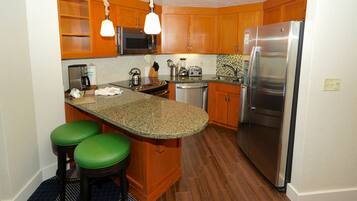 A kitchen with wooden cabinets, a stainless steel refrigerator, a microwave, a stove, and two green bar stools.