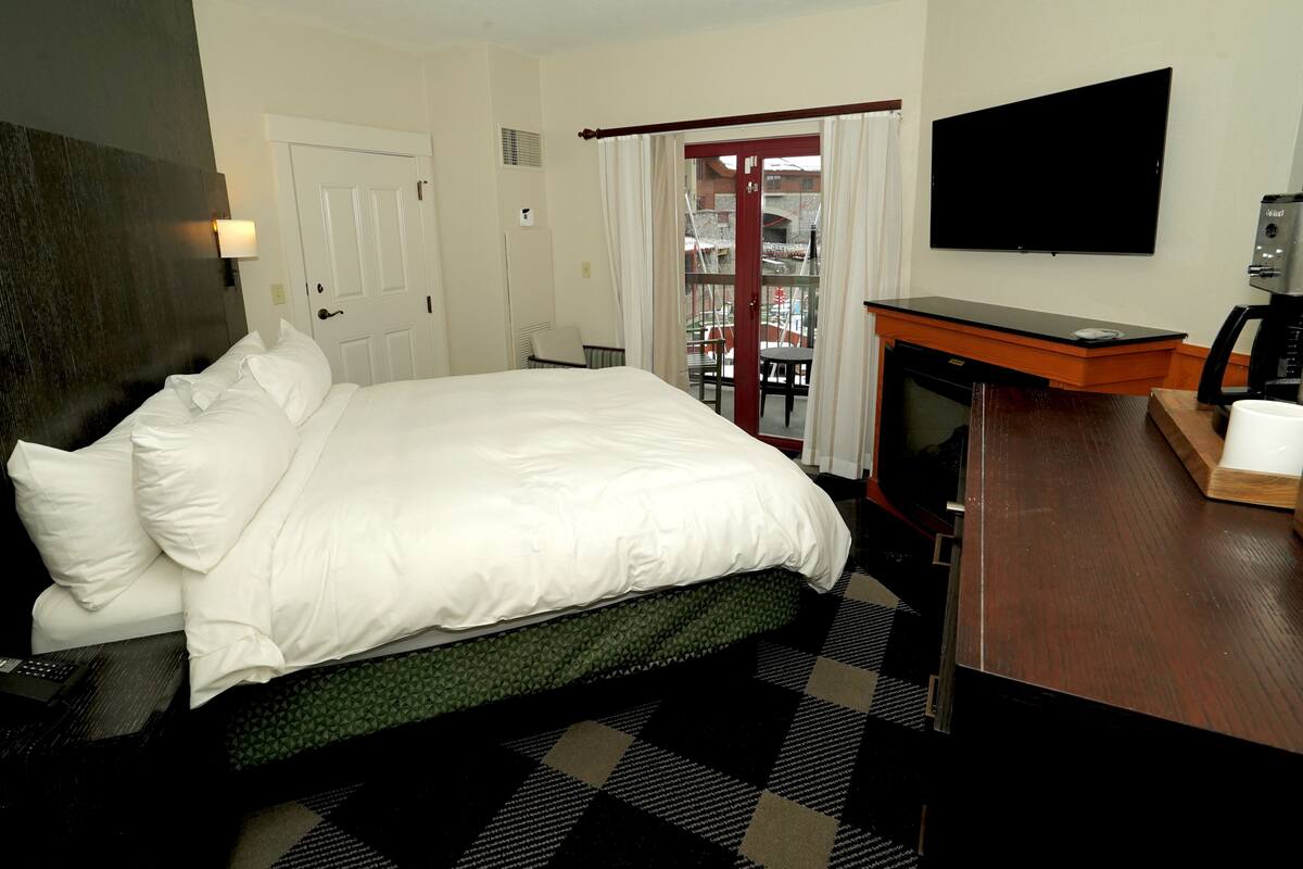 A hotel room with a bed, a television, a desk, and a view of the outside.