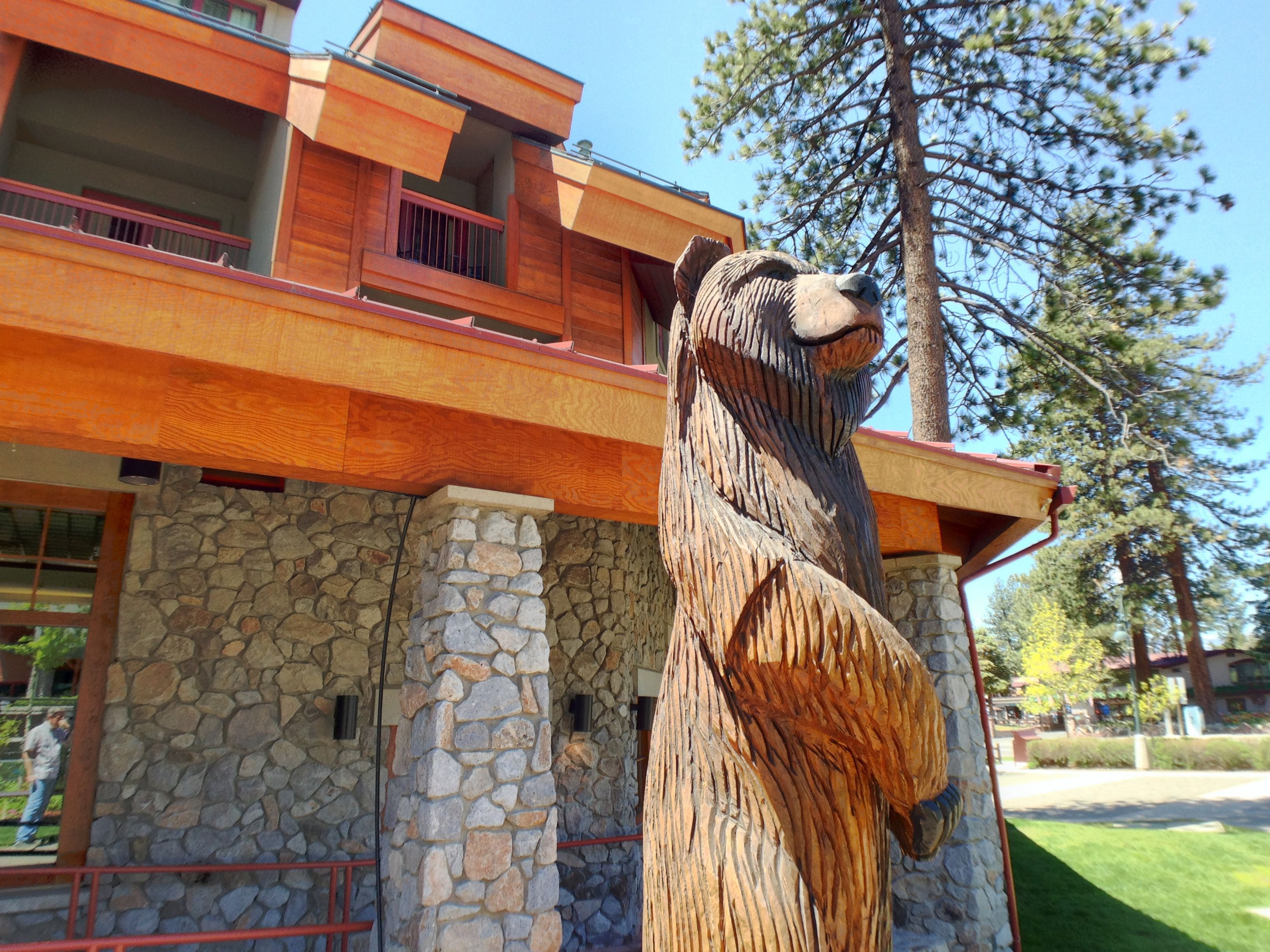 Une sculpture d’ours en bois se trouve devant un bâtiment aux murs de pierre et doté d’un balcon en bois.