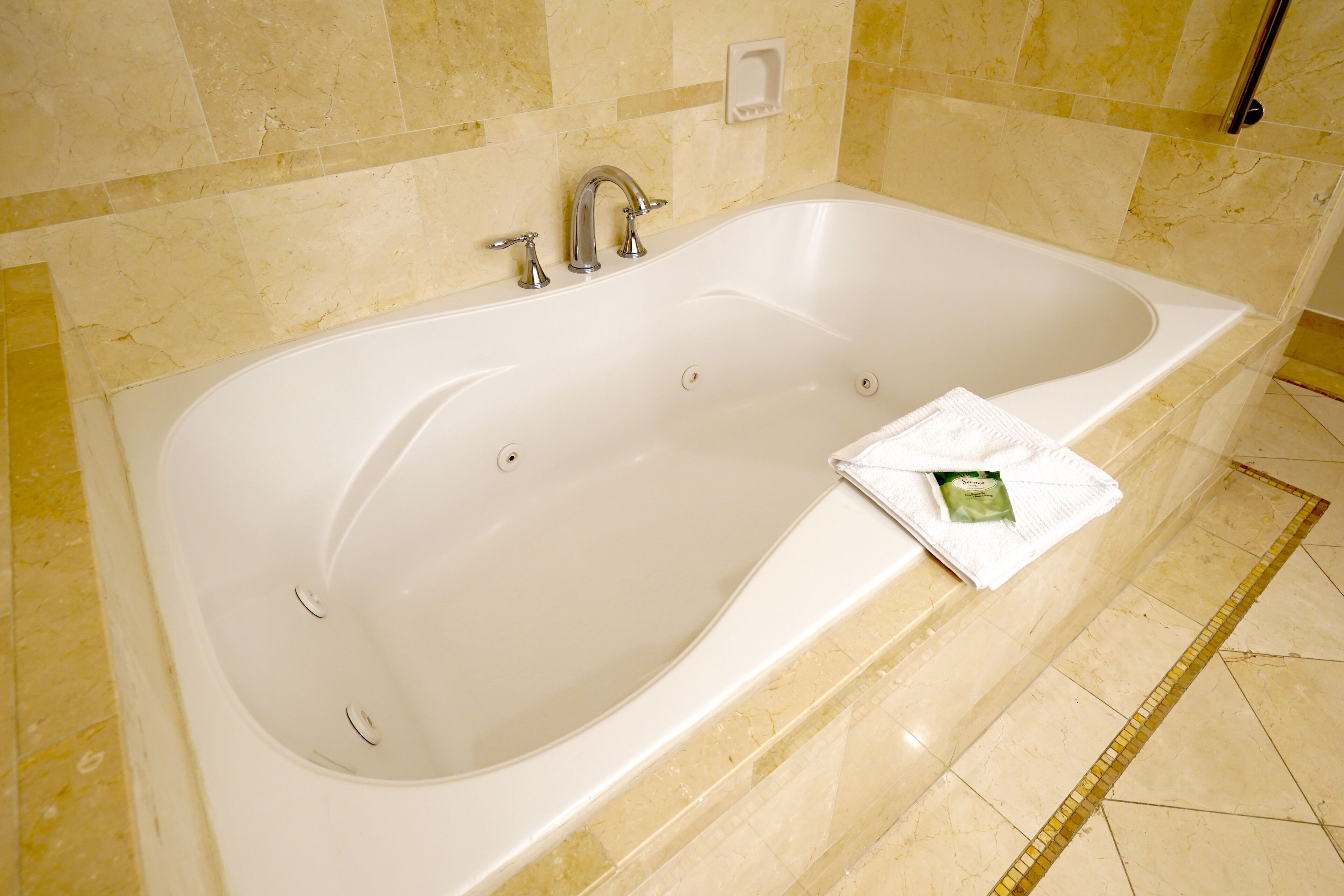 A large, empty bathtub with a single faucet and a towel on the side.