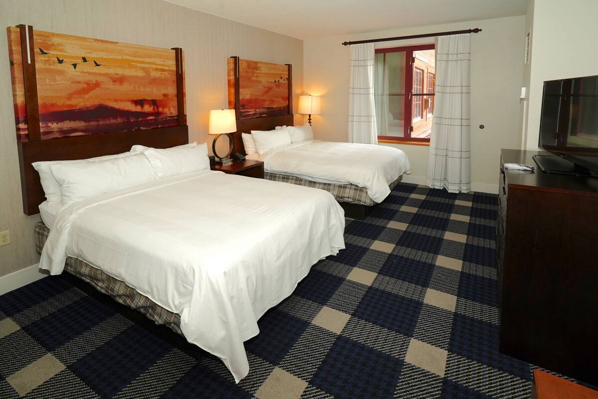 A hotel room with two beds, a checkered floor, a TV, and artwork on the walls.