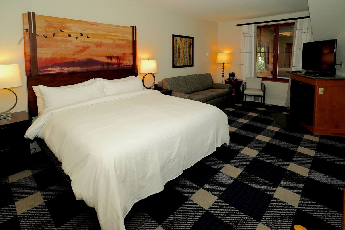 A hotel room with a large bed, a sofa, a desk with a TV, and artwork on the walls.