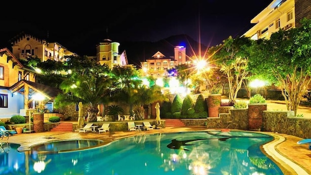A swimming pool surrounded by lounge chairs and palm trees, with a building in the background. - Beachfront Hotel (Ho Chi Minh City)