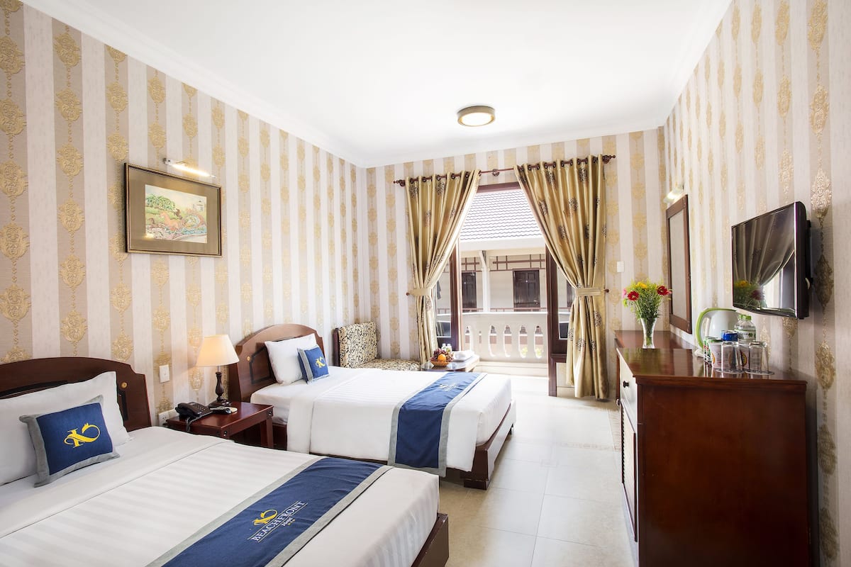 A hotel room with two beds, a desk, a TV, and a balcony with curtains.