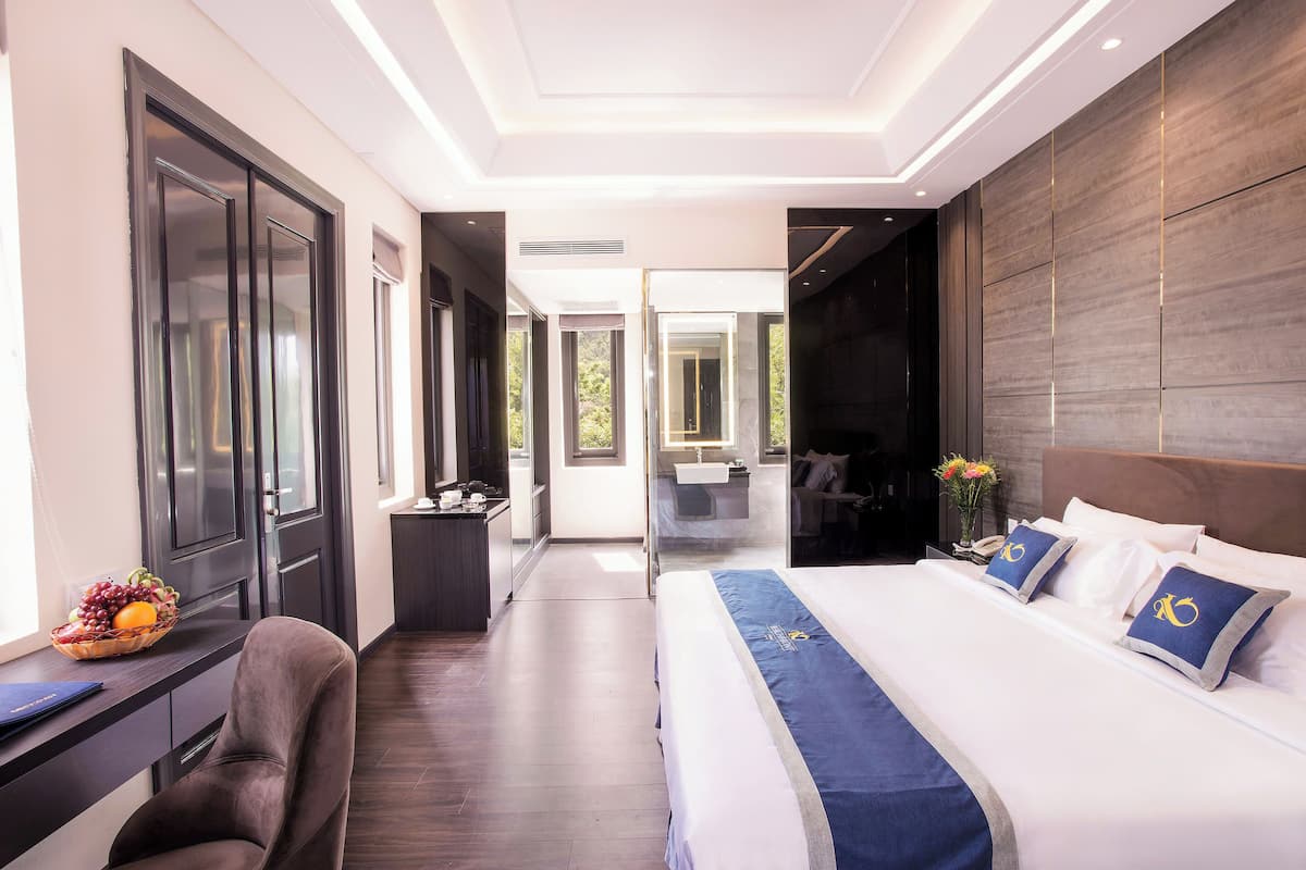 A modern hotel room with a large bed, a desk with a computer, and a view of the outdoors.