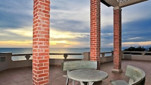 A covered outdoor seating area with brick pillars, a round table, and benches, overlooking a body of water. - Beachfront Hotel (Ho Chi Minh City)
