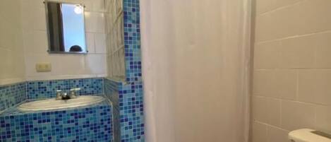 A bathroom with a tiled sink, a shower curtain, a toilet, and a small mirror.