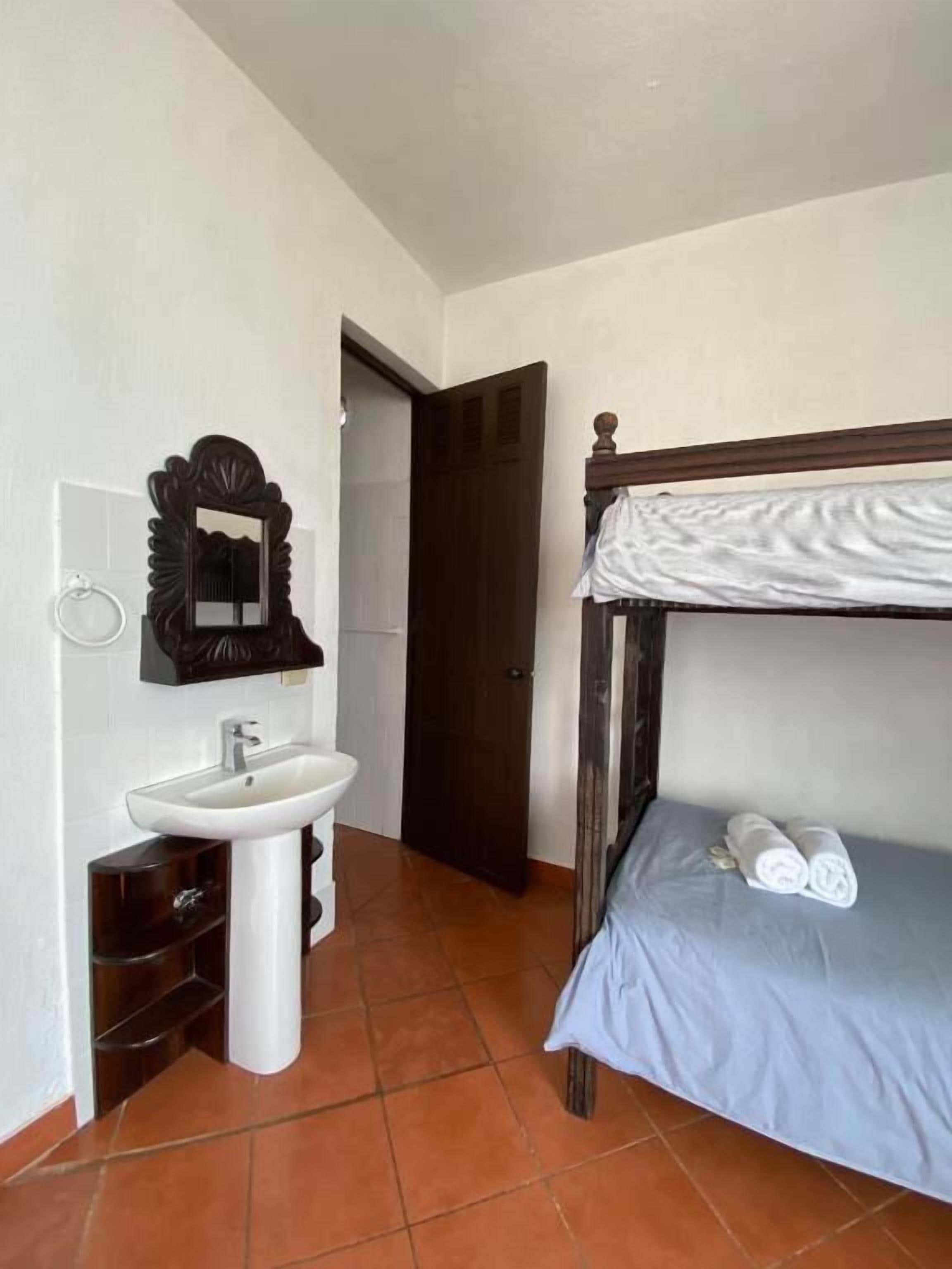 Un dormitorio con una litera, un lavamanos blanco, un espejo y una puerta que da a otra habitación.