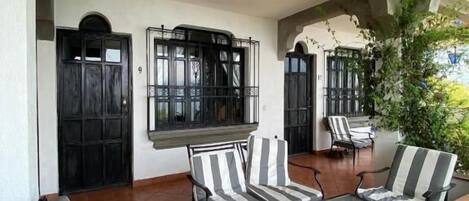 An outdoor patio with striped chairs and a table, a black door, and a hanging light fixture.