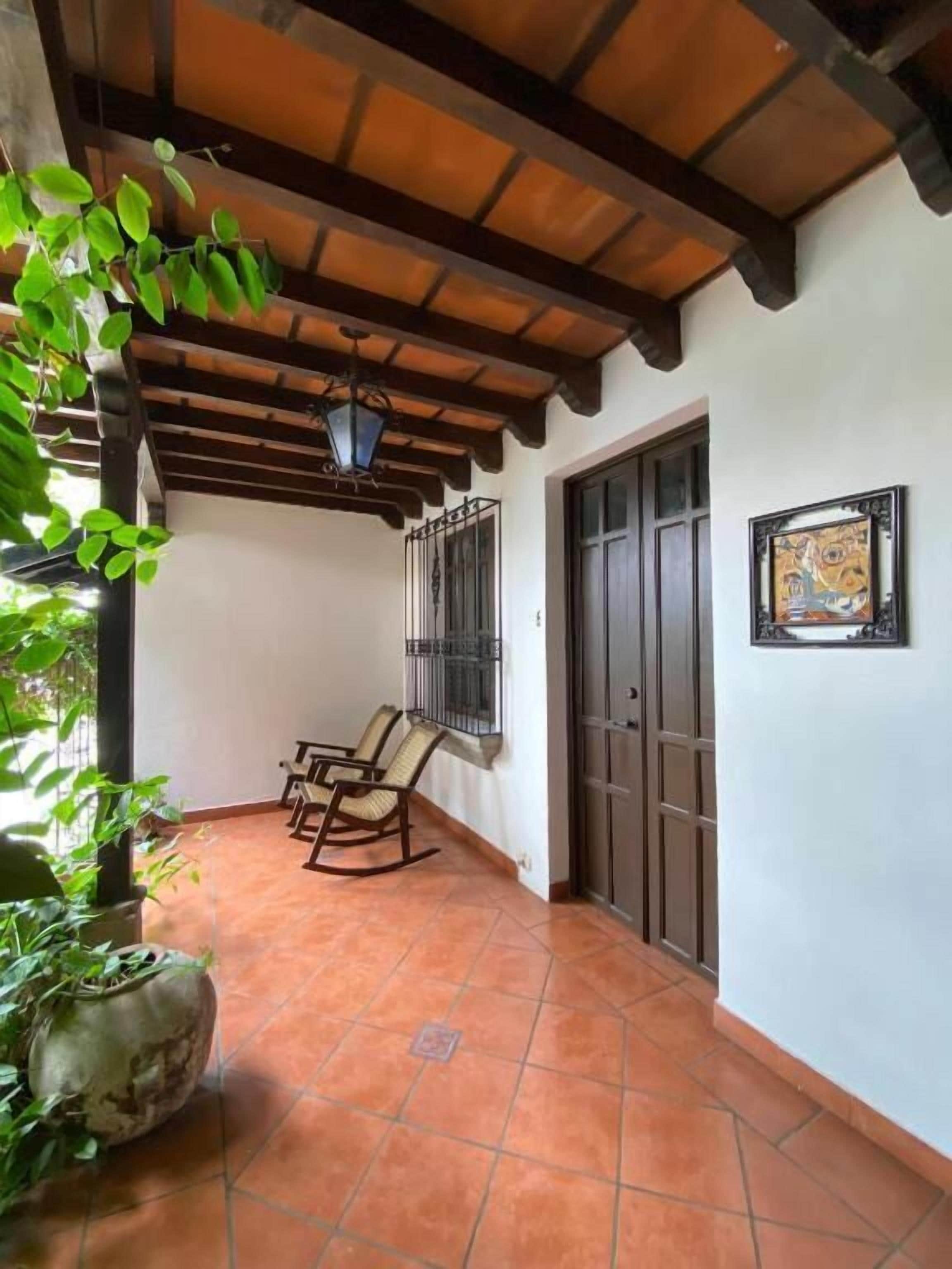 Un patio cubierto con baldosas de terracota, vigas de techo de madera y un conjunto de dos mecedoras.