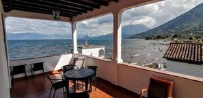 A balcony with a view of the sea and mountains, featuring a table and chairs. - Mikaso Hotel (San Pedro La Laguna)