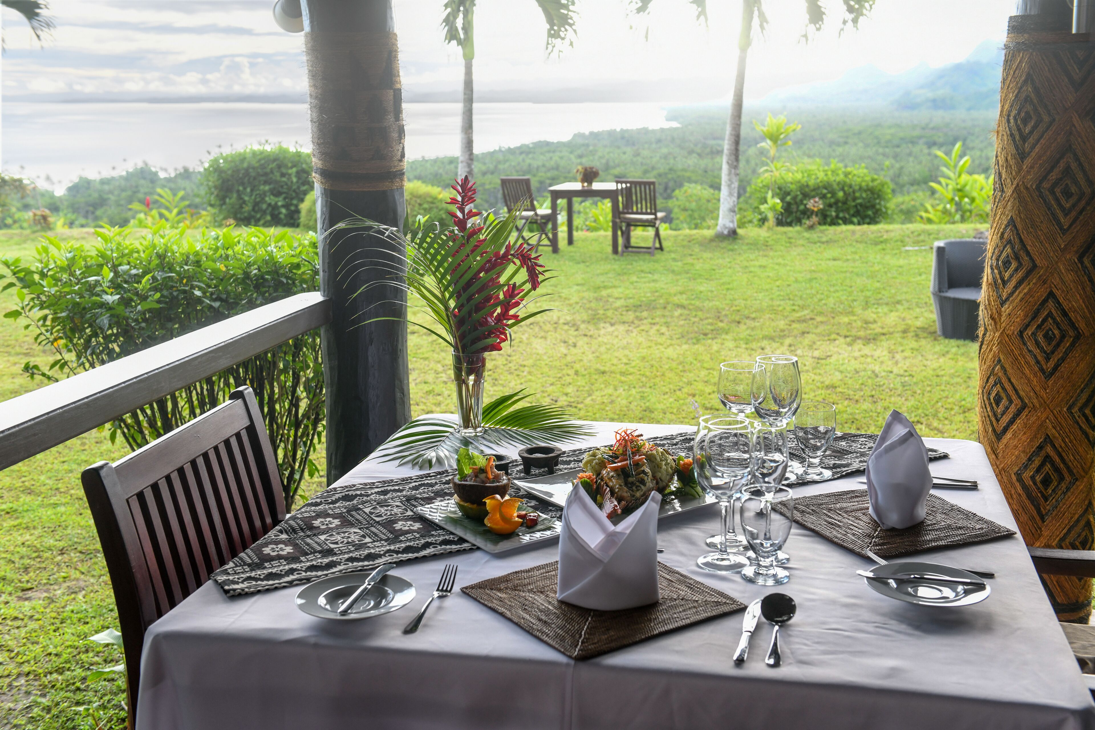 A table set for dining with a view of the ocean and hills.