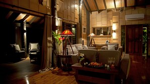 A cozy living room with a wooden floor, a sofa, a coffee table with flowers, and a lamp. - Emaho Sekawa Resort (Savusavu)