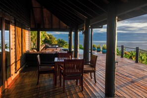 A wooden deck with a table and chairs, overlooking a body of water and greenery. - Emaho Sekawa Resort (Savusavu)