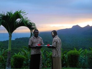Two individuals in a tropical setting with a mountainous backdrop, one holding a plate with food. - Emaho Sekawa Resort (Savusavu)
