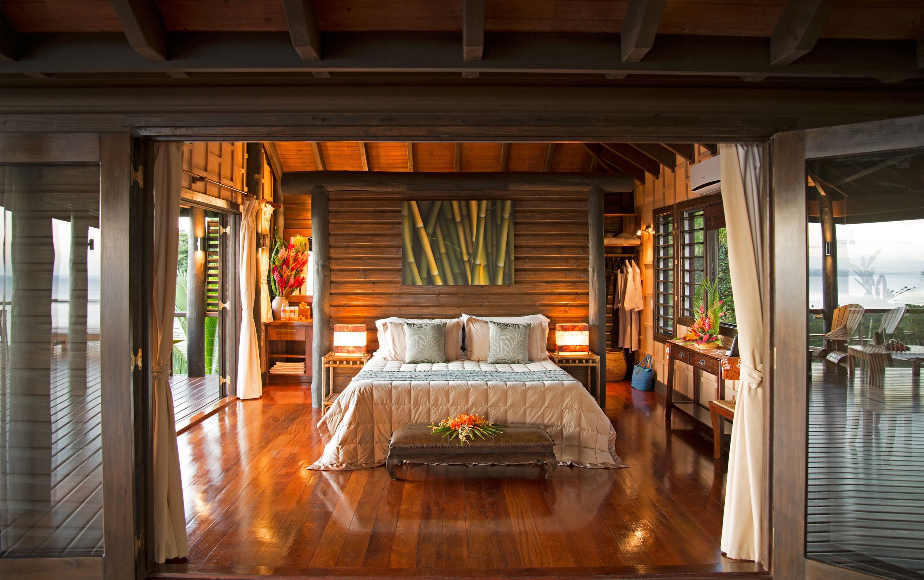 A spacious bedroom with a large bed, wooden walls, and a view of the sea.