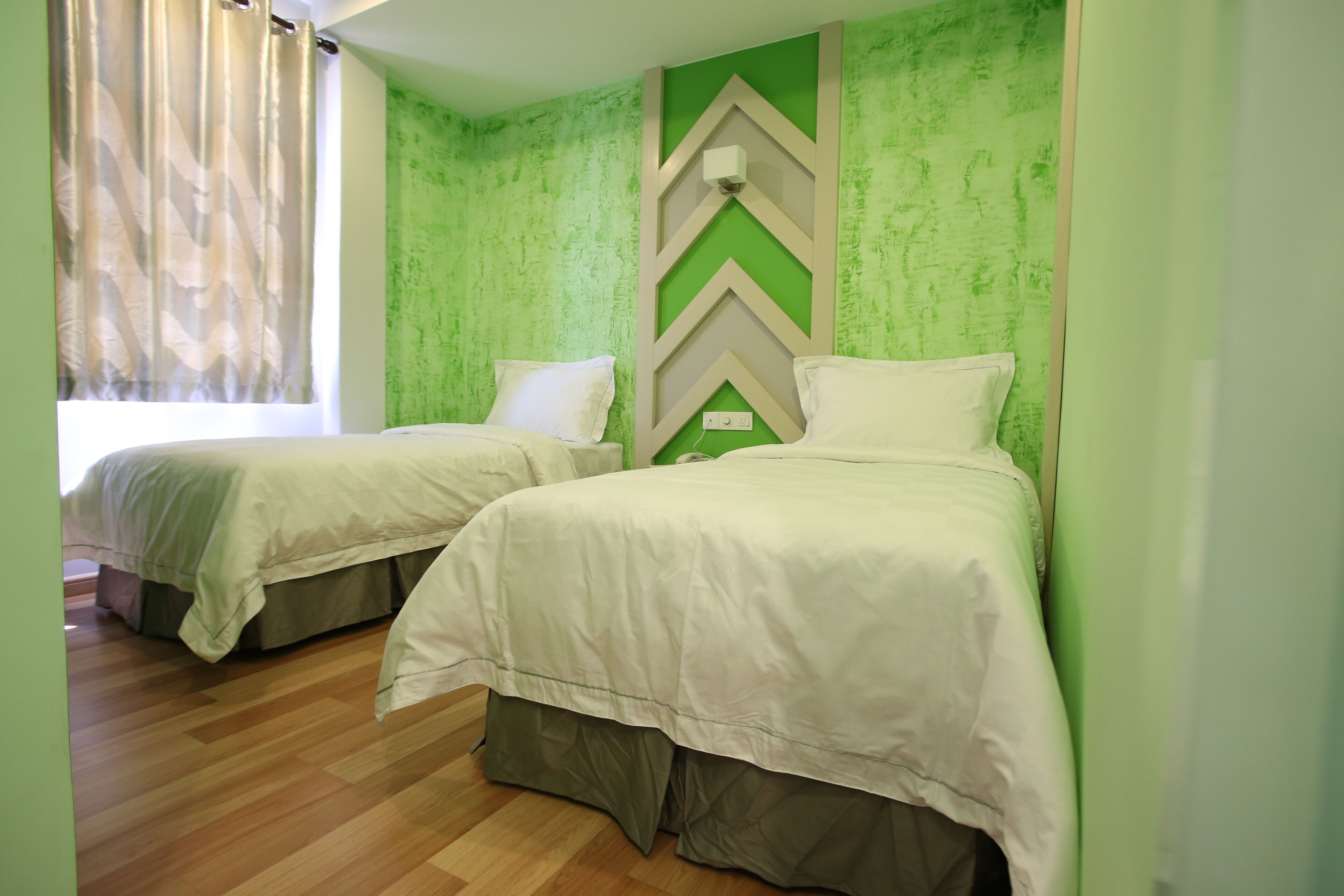 Zwei Einzelbetten mit weißer Bettwäsche in einem Zimmer mit grüne Wandtextur und Holzboden.