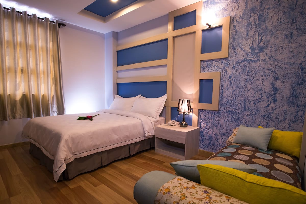 A bedroom with a bed, bedside table, lamp, and a patterned sofa.