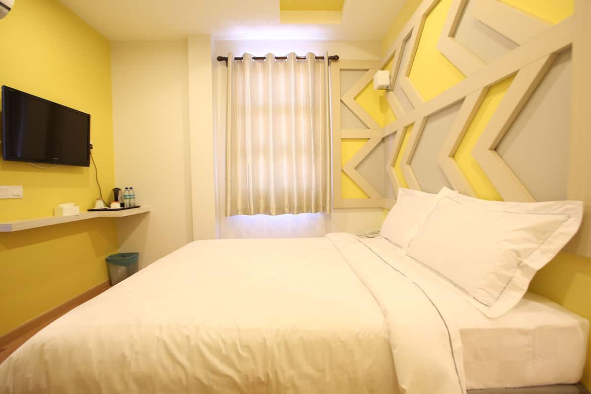 A hotel room with a bed, a television mounted on the wall, a window with curtains, and a decorative wall panel.
