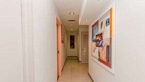 Un couloir aux murs blancs, doté d’un sol carrelé et d’une porte au fond.
