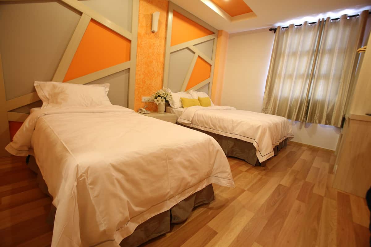 A hotel room with two beds, wooden flooring, and a modern design with orange accents.