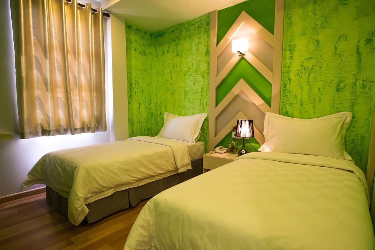 A hotel room with two beds, a nightstand with a lamp, and a green textured wall.