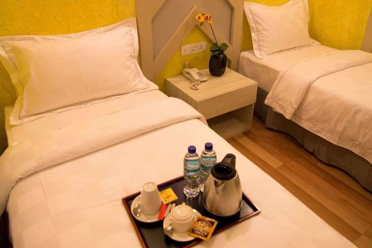 A hotel room with two beds, a nightstand with a phone, a vase with flowers, and a tray with breakfast items.