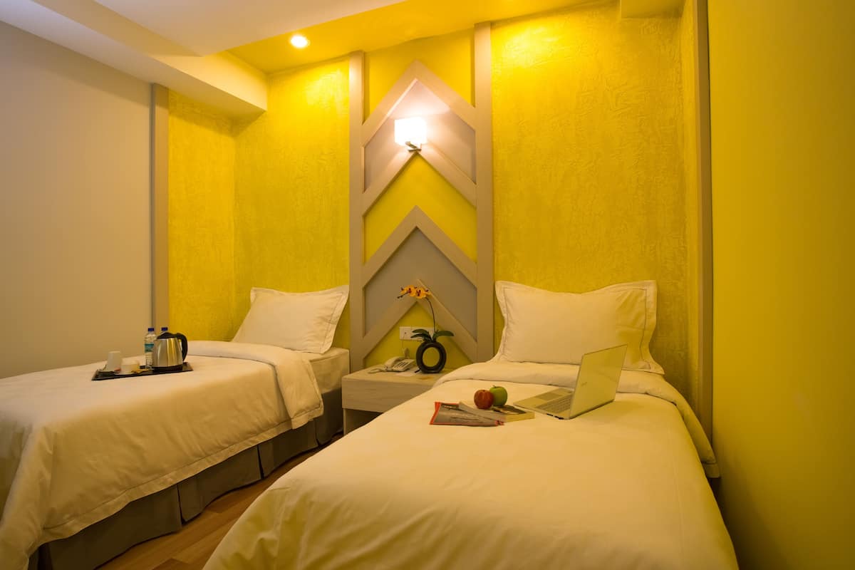A hotel room with two beds, a nightstand with a lamp, a telephone, and a laptop on one bed.