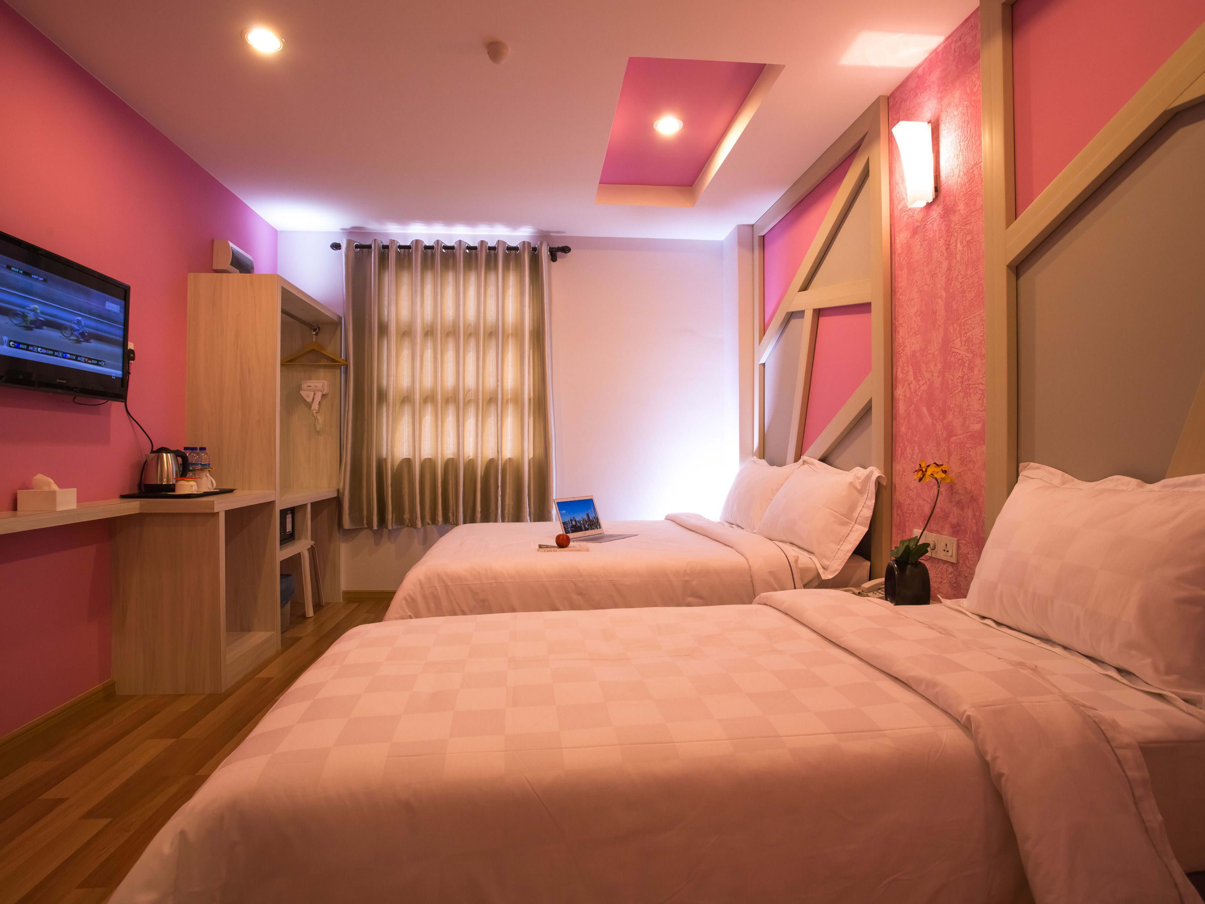 Habitación de hotel con dos camas, un televisor, un escritorio con tetera y una ventana con cortinas.