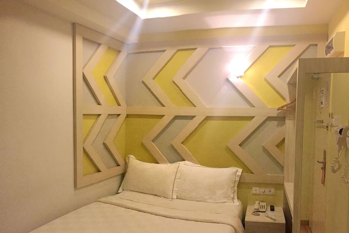 A hotel room with a bed, a nightstand with a phone, and a wardrobe.