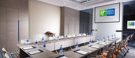 Un salón de conferencias con una mesa larga, sillas, botellas de agua y una pantalla mostrando el logotipo de Holiday Inn Express.