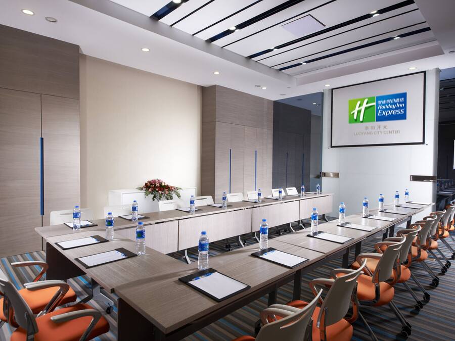 Un salón de conferencias con una mesa larga, sillas, botellas de agua y una pantalla mostrando el logotipo de Holiday Inn Express.