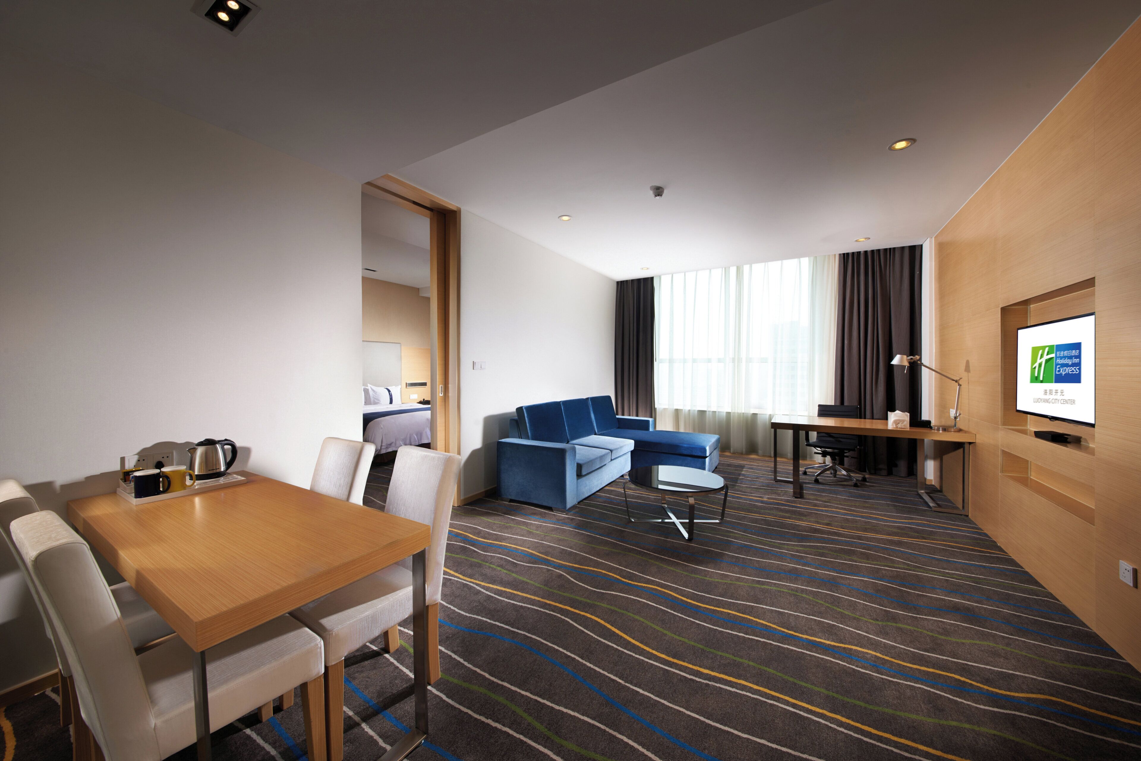 A hotel room with a dining area, a sofa, a TV, and a window with curtains.
