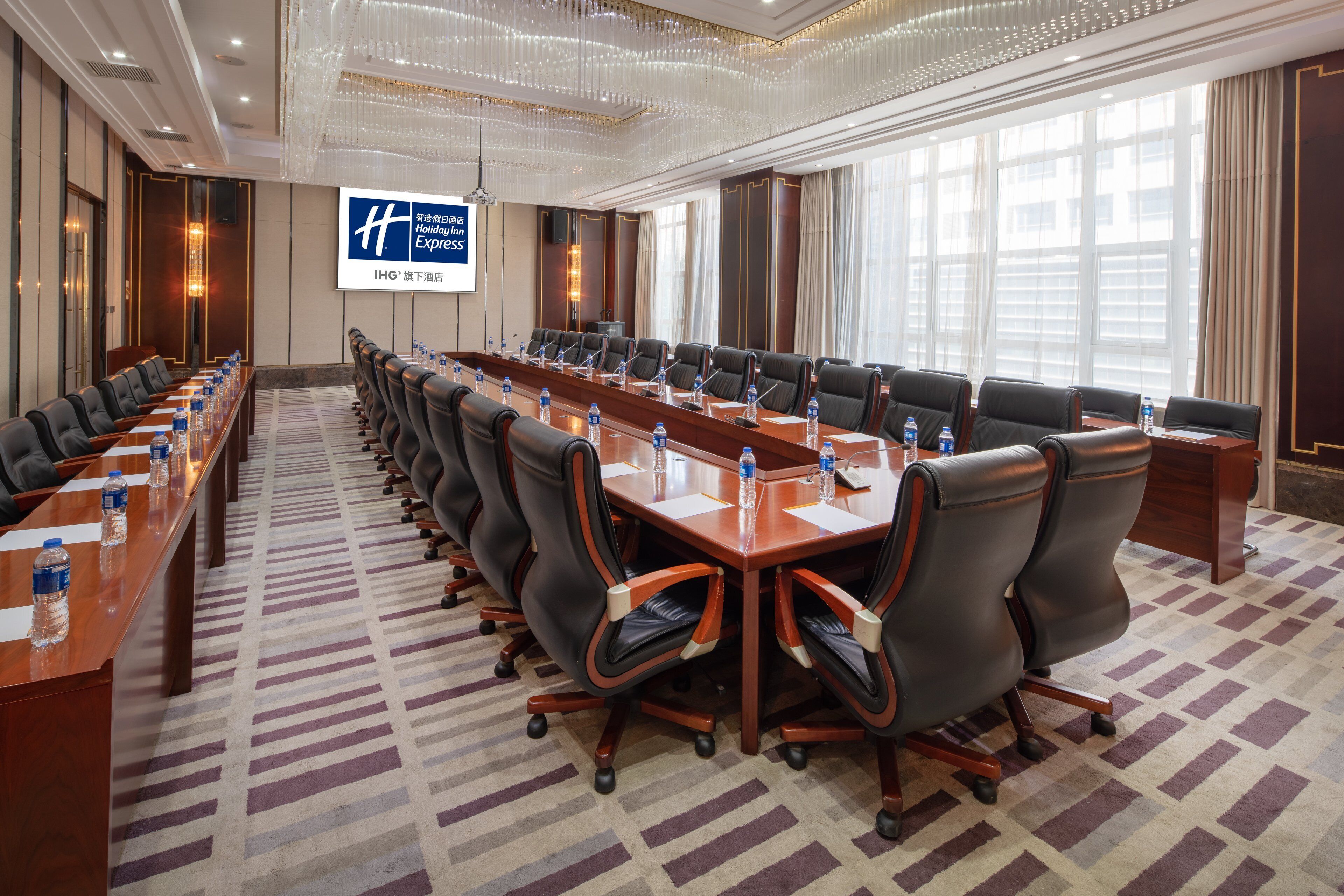 Un salón de conferencias con una larga mesa, varias sillas, botellas de agua y una pantalla mostrando el logotipo de Holiday Inn Express.