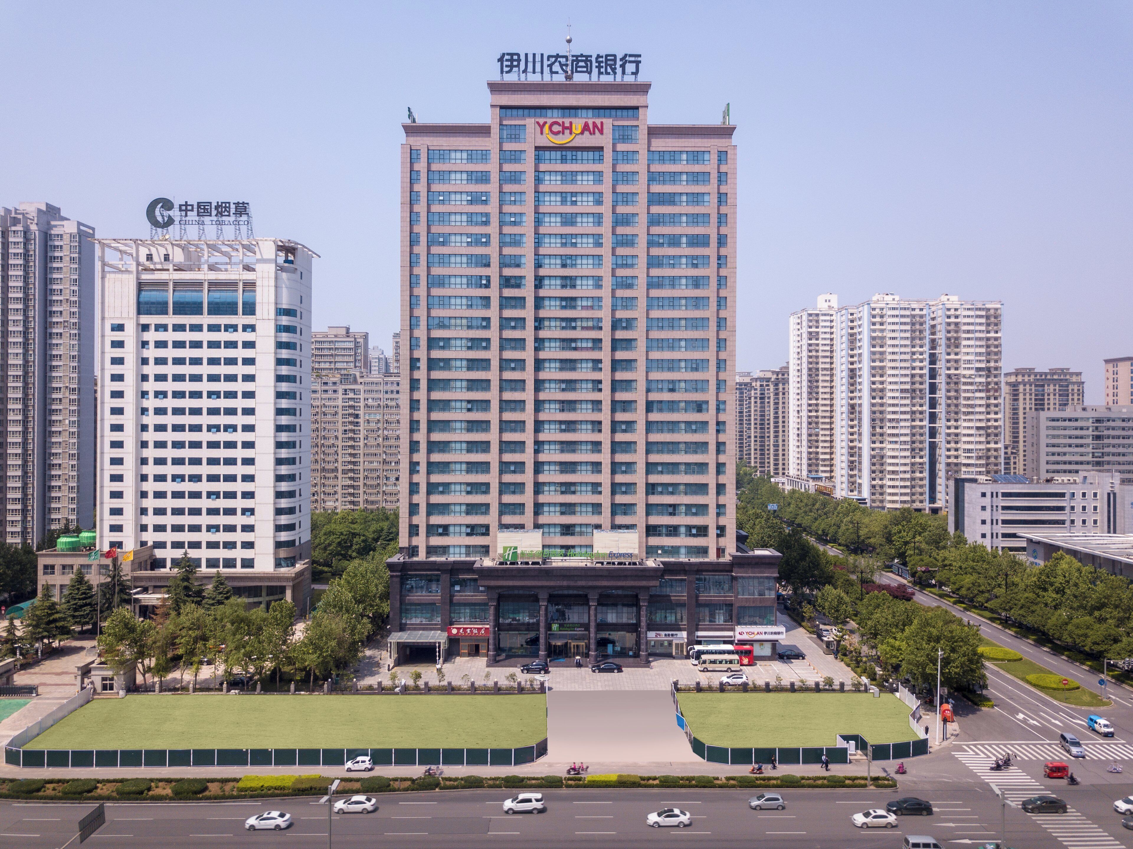 A high-rise building with multiple floors, a prominent sign at the top, and a surrounding urban environment with other buildings and a road.