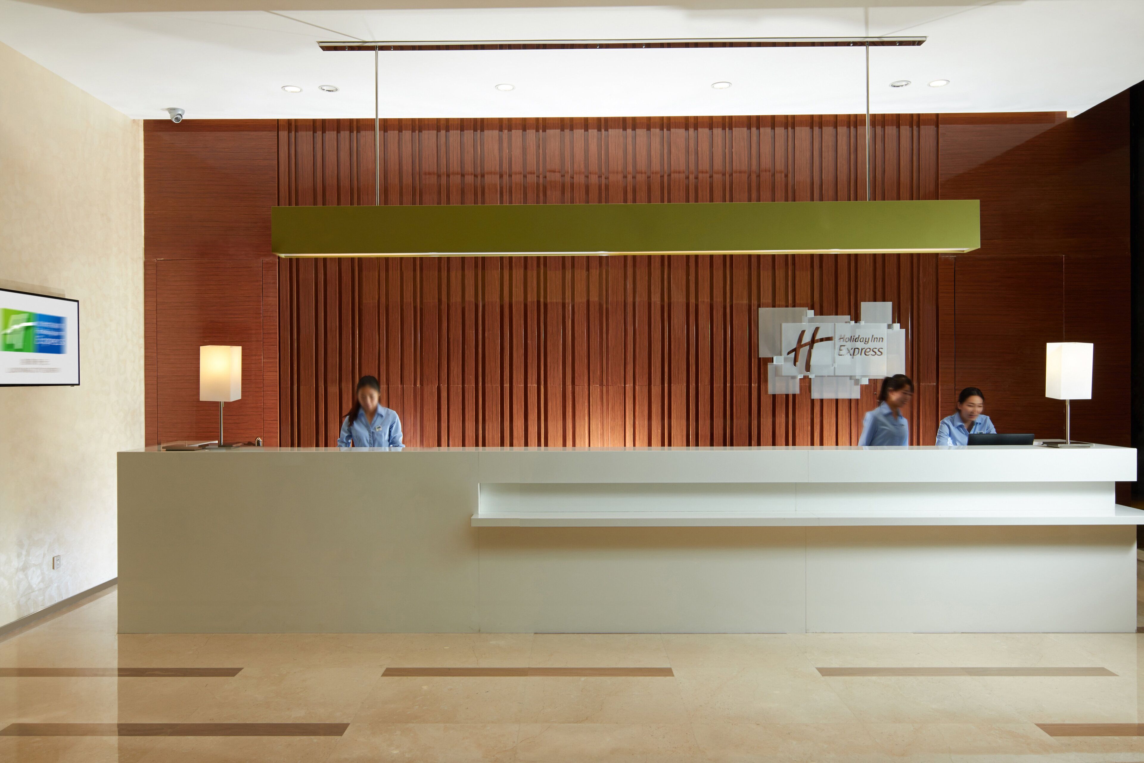 A hotel reception desk with a modern design, a sign indicating it's a Holiday Inn Express, and a security camera above.