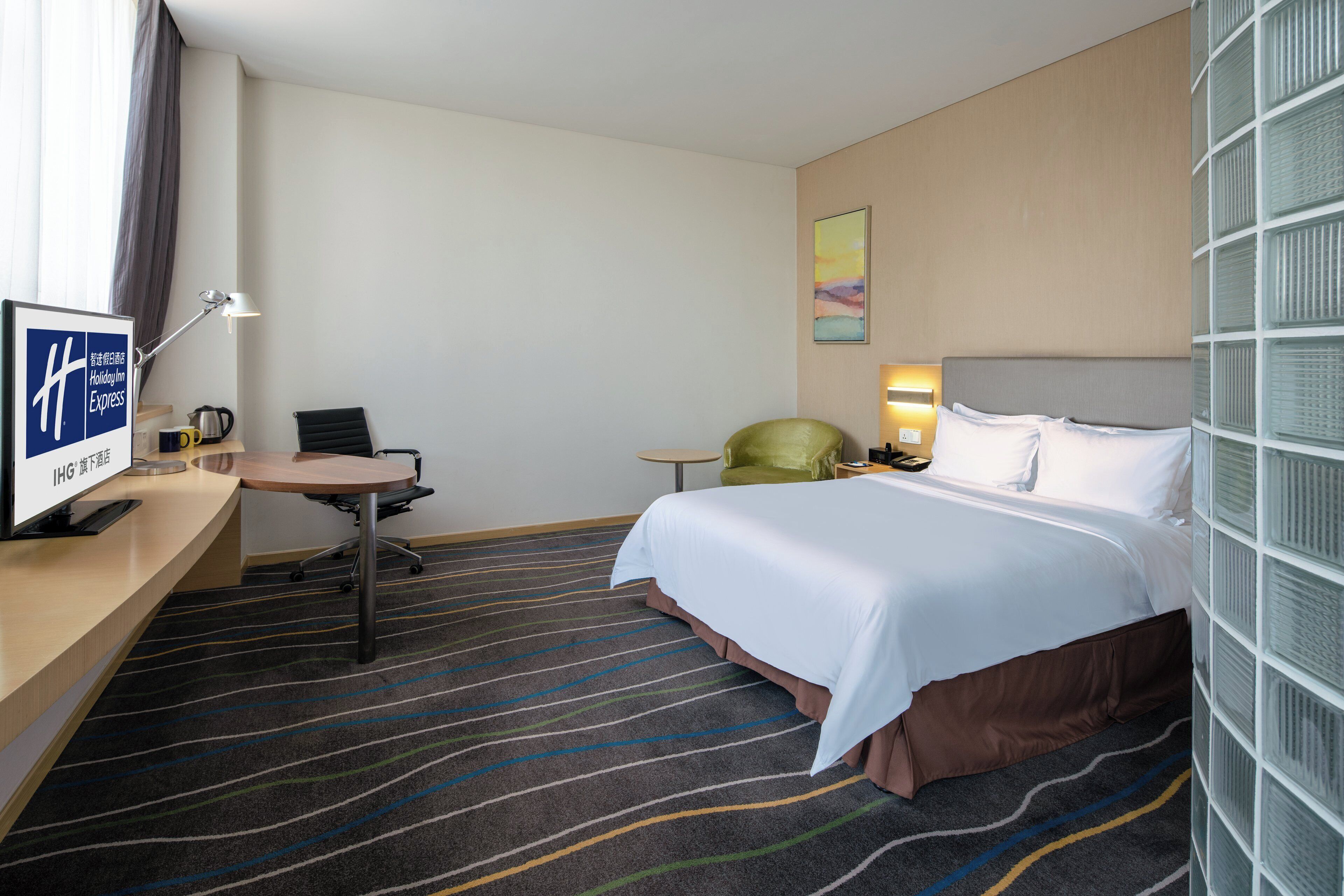 Habitación de hotel con cama, escritorio, silla, televisor y ventana con cortinas.