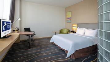 Habitación de hotel con cama, escritorio, silla, televisor y ventana con cortinas.