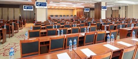 A conference room with rows of tables and chairs, equipped with water bottles, and signs indicating the Holiday Inn Express location.