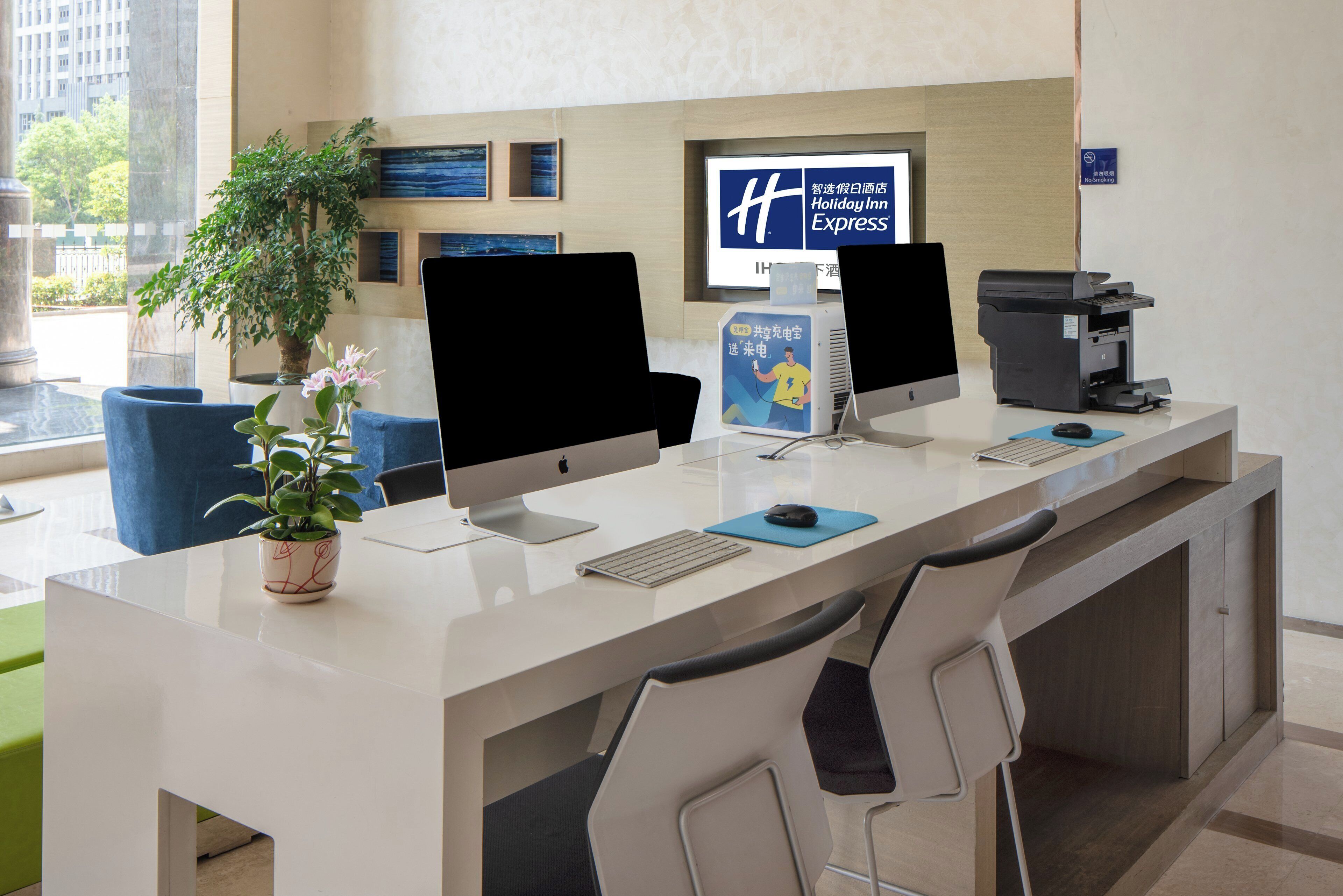 A hotel reception desk with two monitors, a computer, a printer, and a sign for Holiday Inn Express.