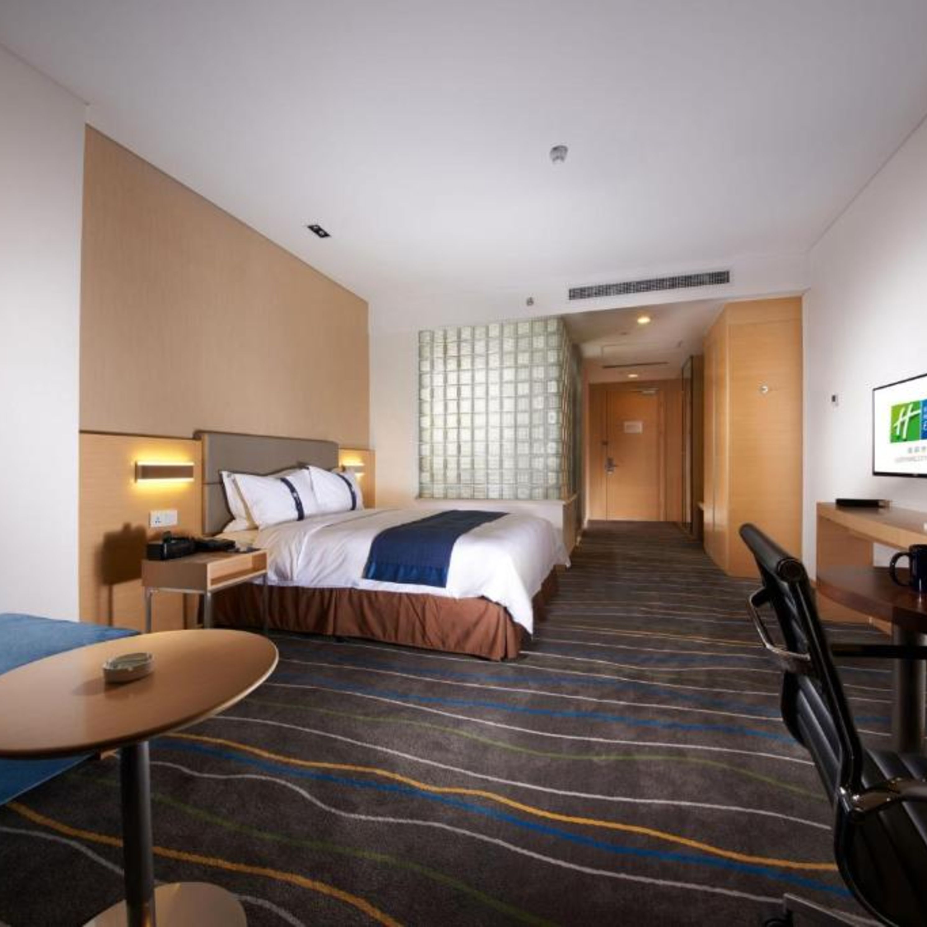 A hotel room with a bed, bedside table, lamp, desk, chair, and a television.