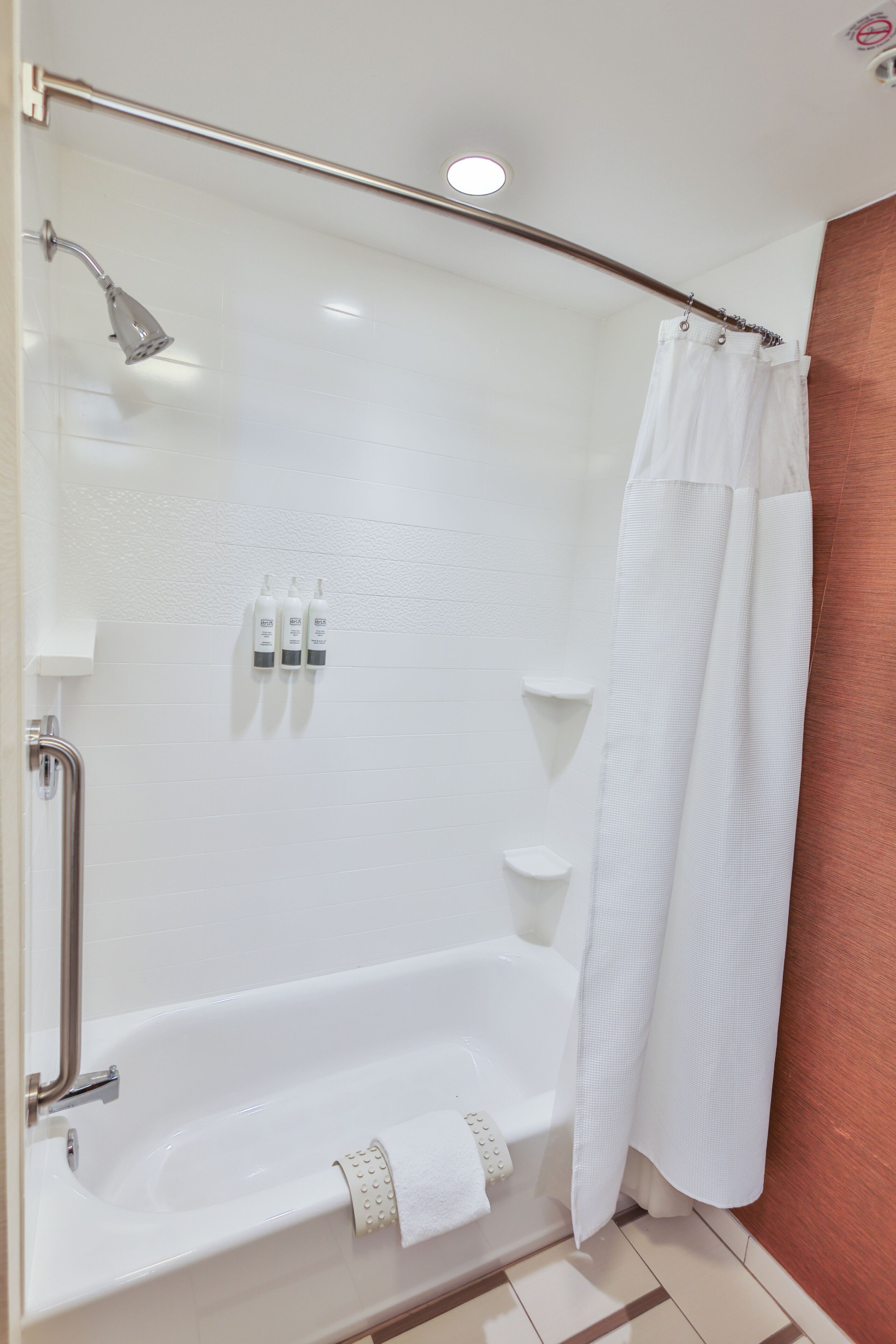 A shower with a handheld showerhead, a glass door, and a white shower curtain.