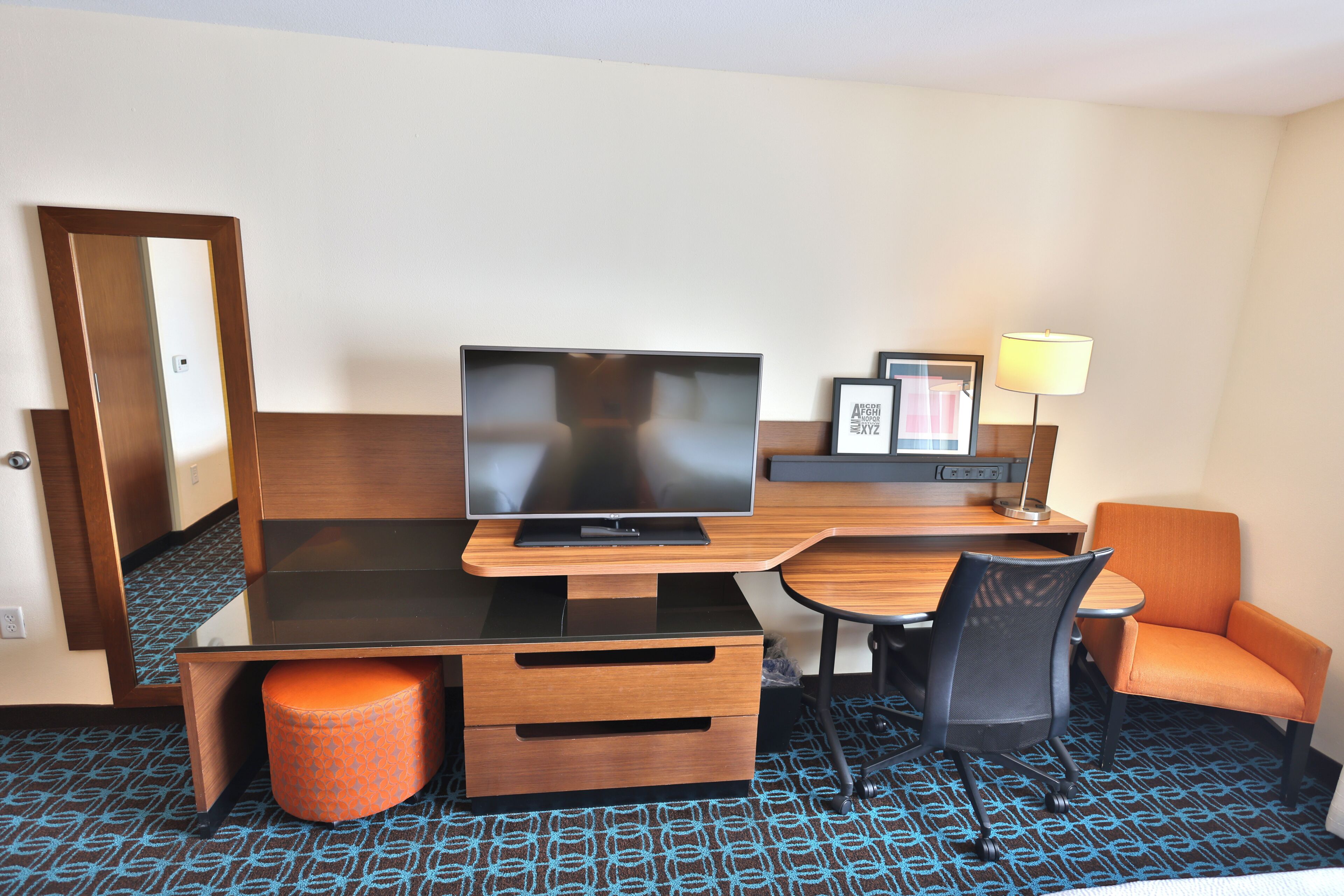 Et hotelværelse med seng, tv, skrivebord, stol og lampe.