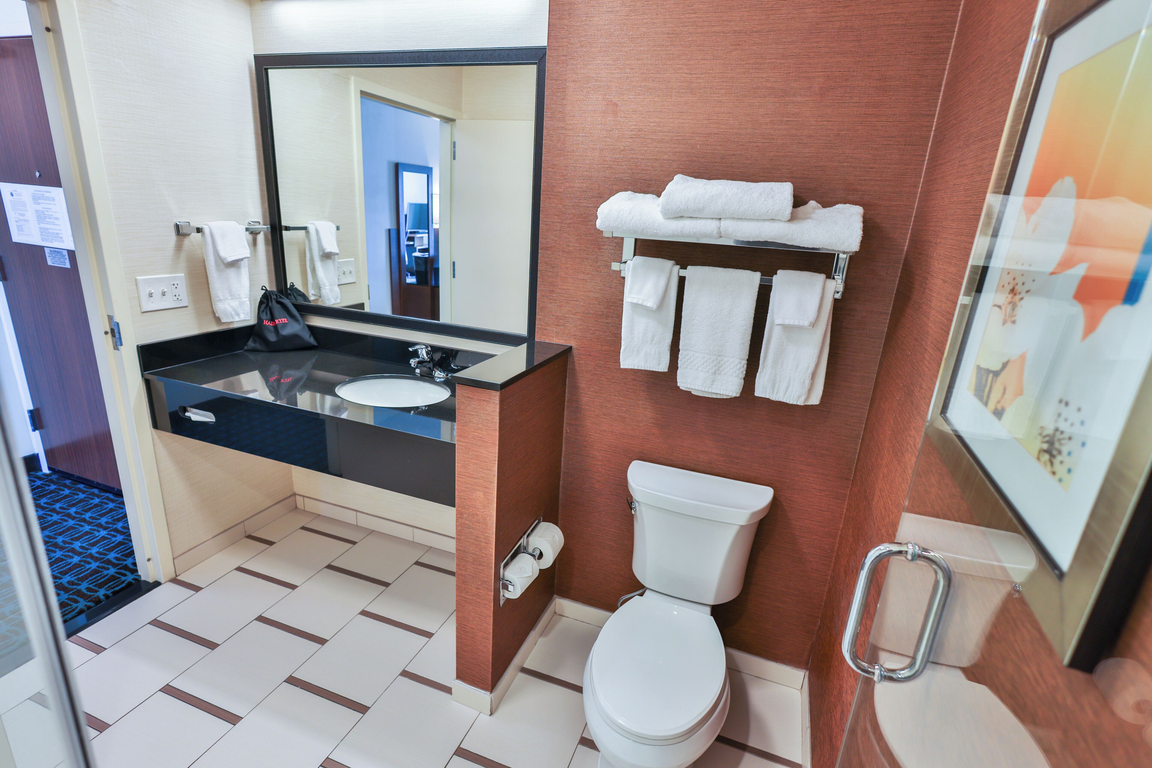 A hotel bathroom with a sink, mirror, toilet, and towel rack.