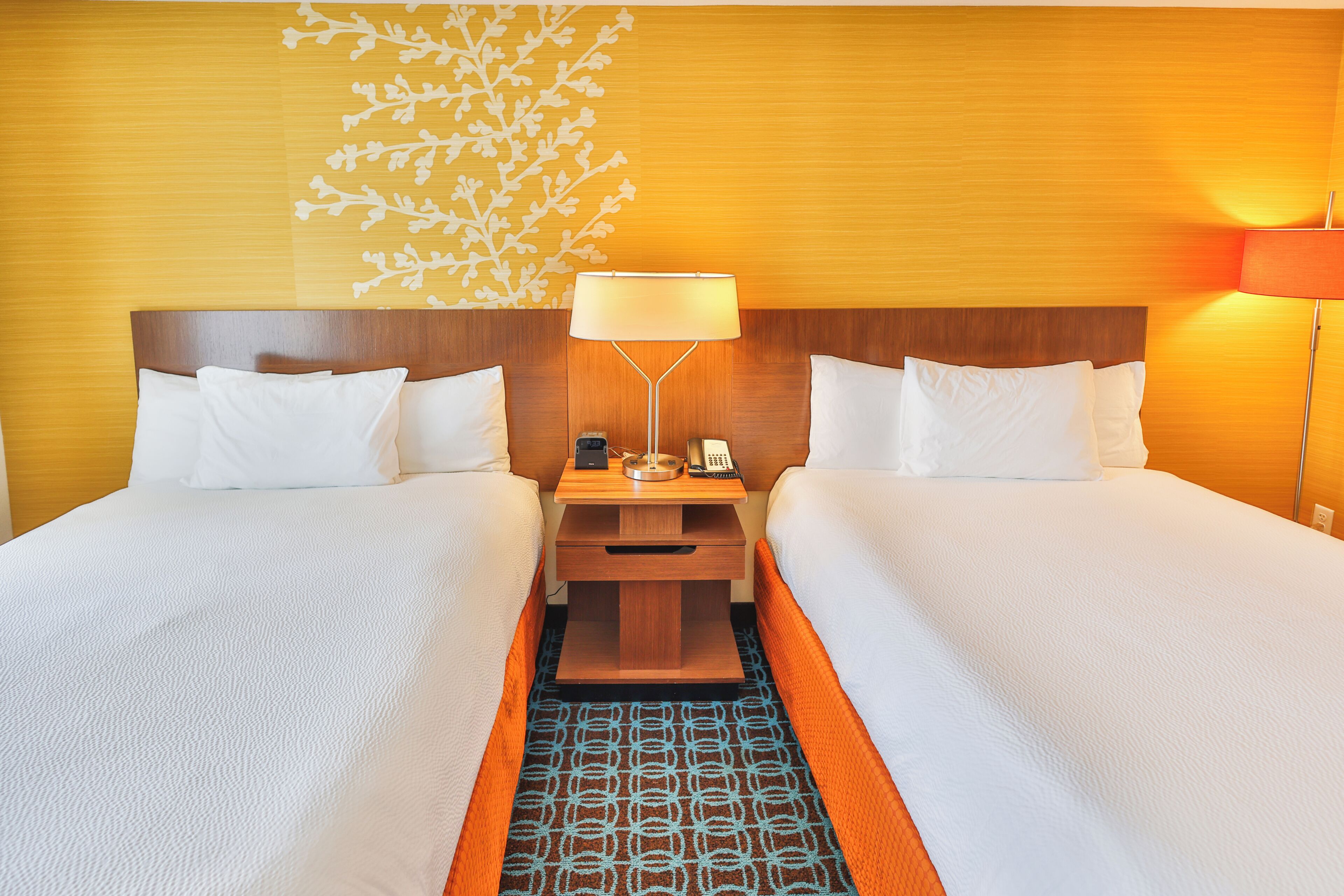 A hotel room with two beds, a nightstand with a lamp, a phone, and a decorative wall piece.