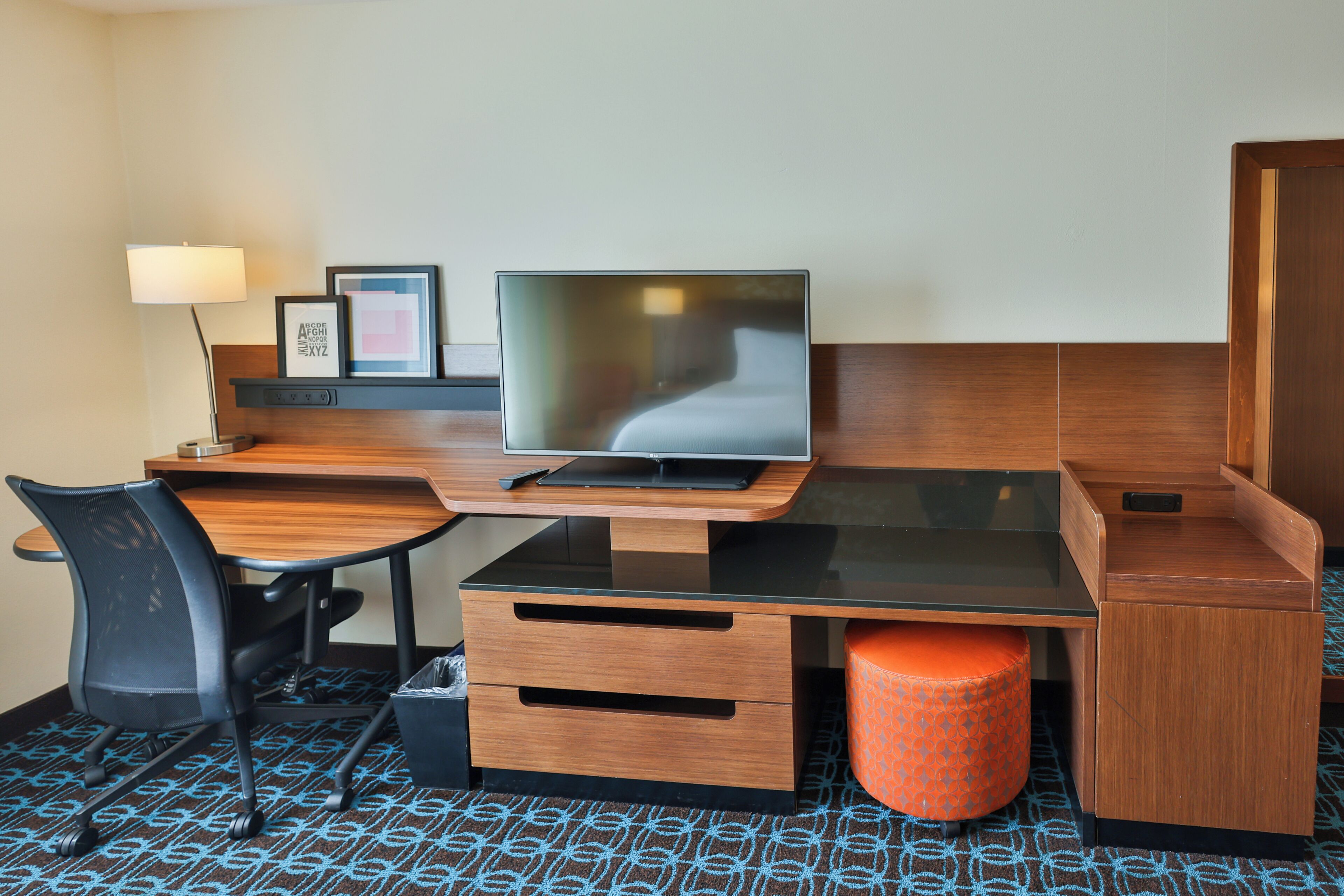 Habitación de hotel con escritorio de madera, televisión, silla, lámpara y cesto de basura.
