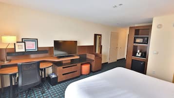 Quarto de hotel com cama, escrivaninha, cadeira, televisão, micro-ondas e pequeno frigorífico.
