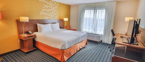 A hotel room with a bed, bedside tables, a desk, a chair, a mirror, and a window with curtains.