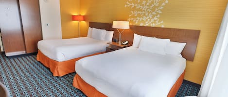 A hotel room with two beds, a nightstand, a lamp, and a wall with a floral pattern.