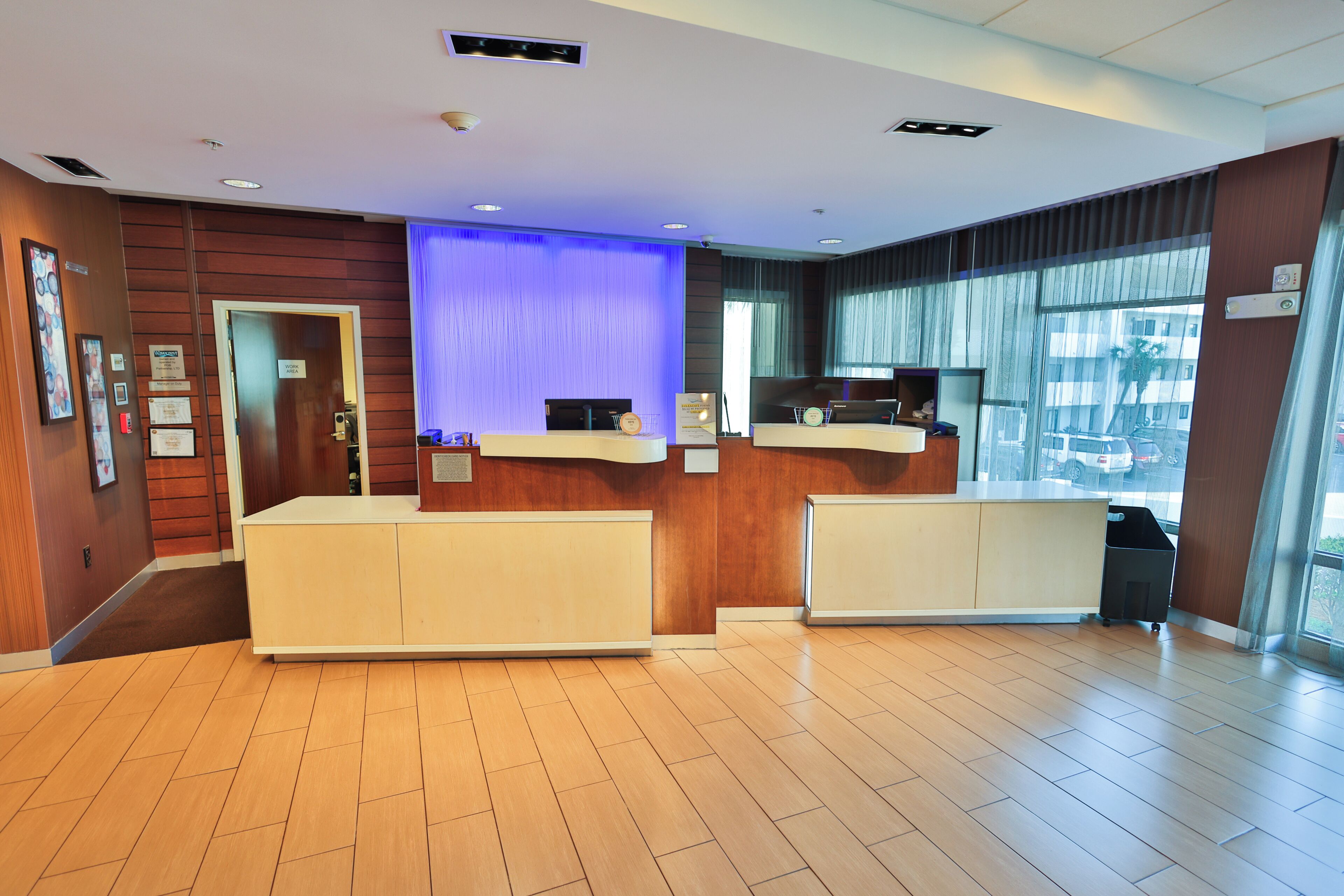 A reception area with a wooden reception desk, a blue accent wall, and a view of the outside through large windows.